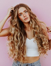 A photo of Sally Lucas posing in jeans and a white crop top with her hand in her long, wavy hair.
