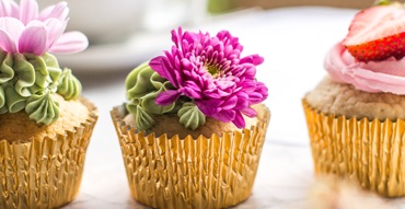 Cupcakes with golden wrappers and decorated with cacti made of icing rest on a table.