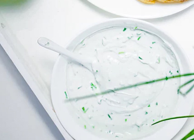 A bowl of tzatziki sauce with a spoon in it rests on a white platter.