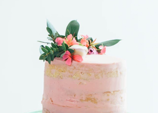 A rustic pink cake decorated with flowers and leaves.